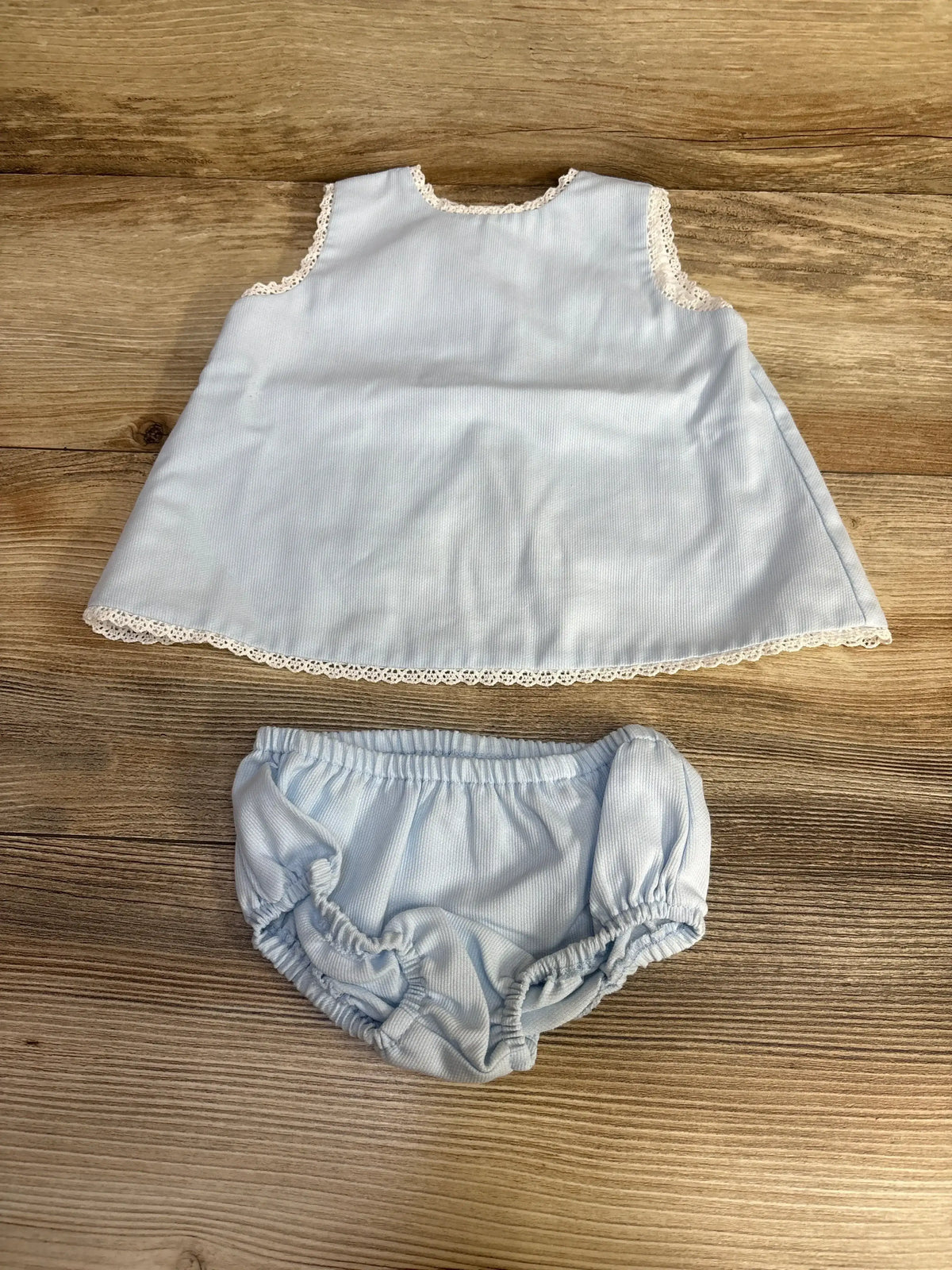 Flat lay of blue 2-piece baby swing set with lace-trim sleeveless top and matching elastic-waist bloomers on wood background
