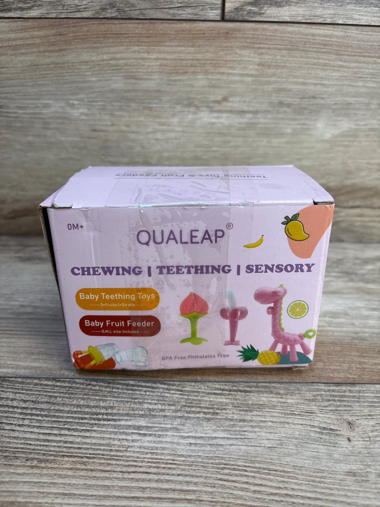 Box of Qualeap baby teething toys and fruit feeder, pink packaging on wood background