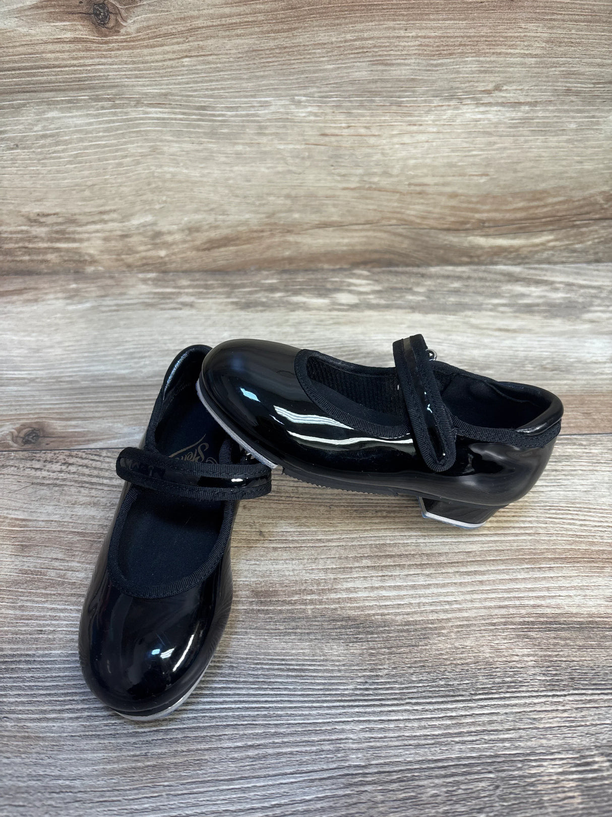 Kids black patent leather tap shoes with straps on wood floor