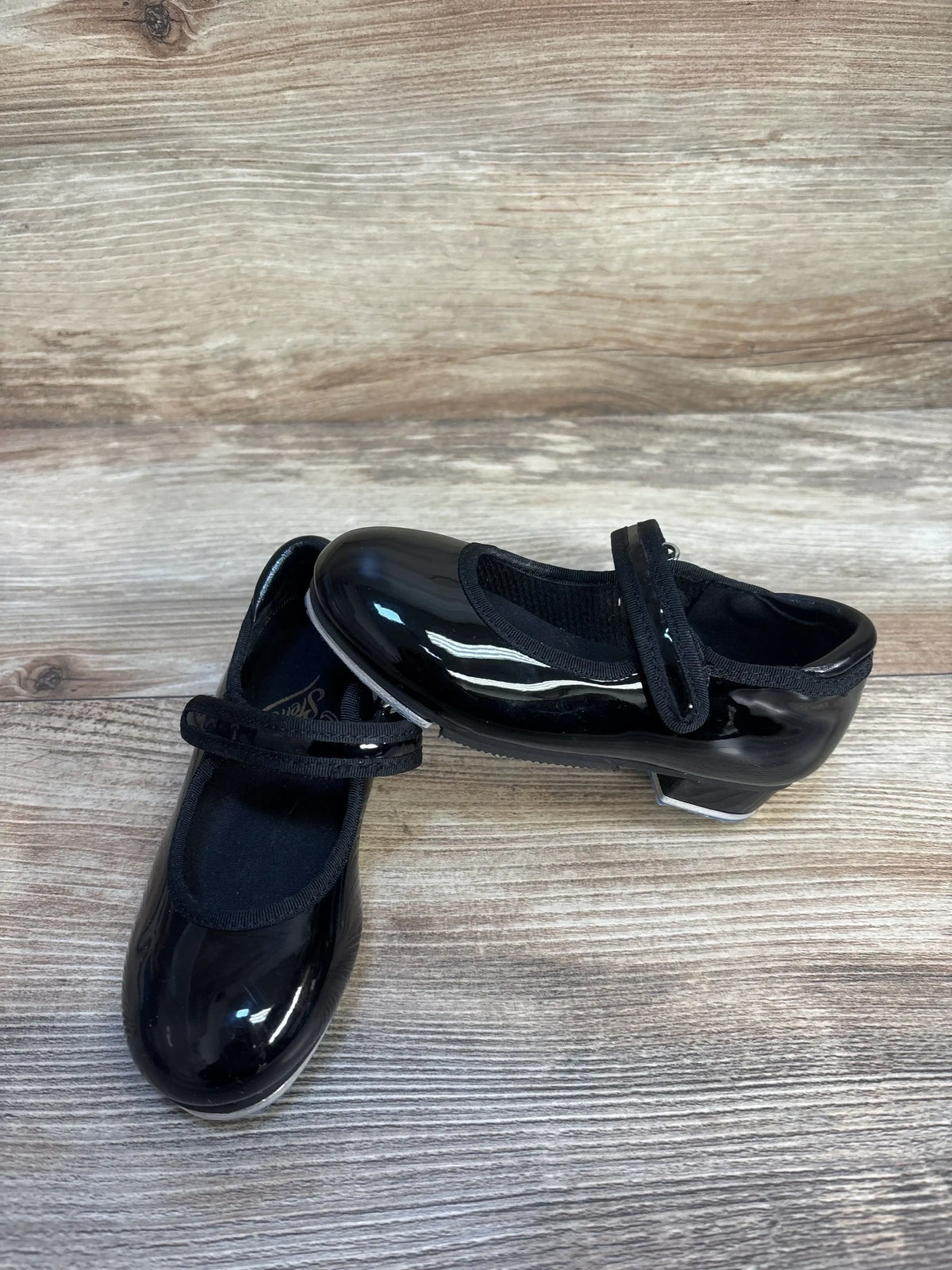 Kids black patent leather tap shoes with straps on wood floor