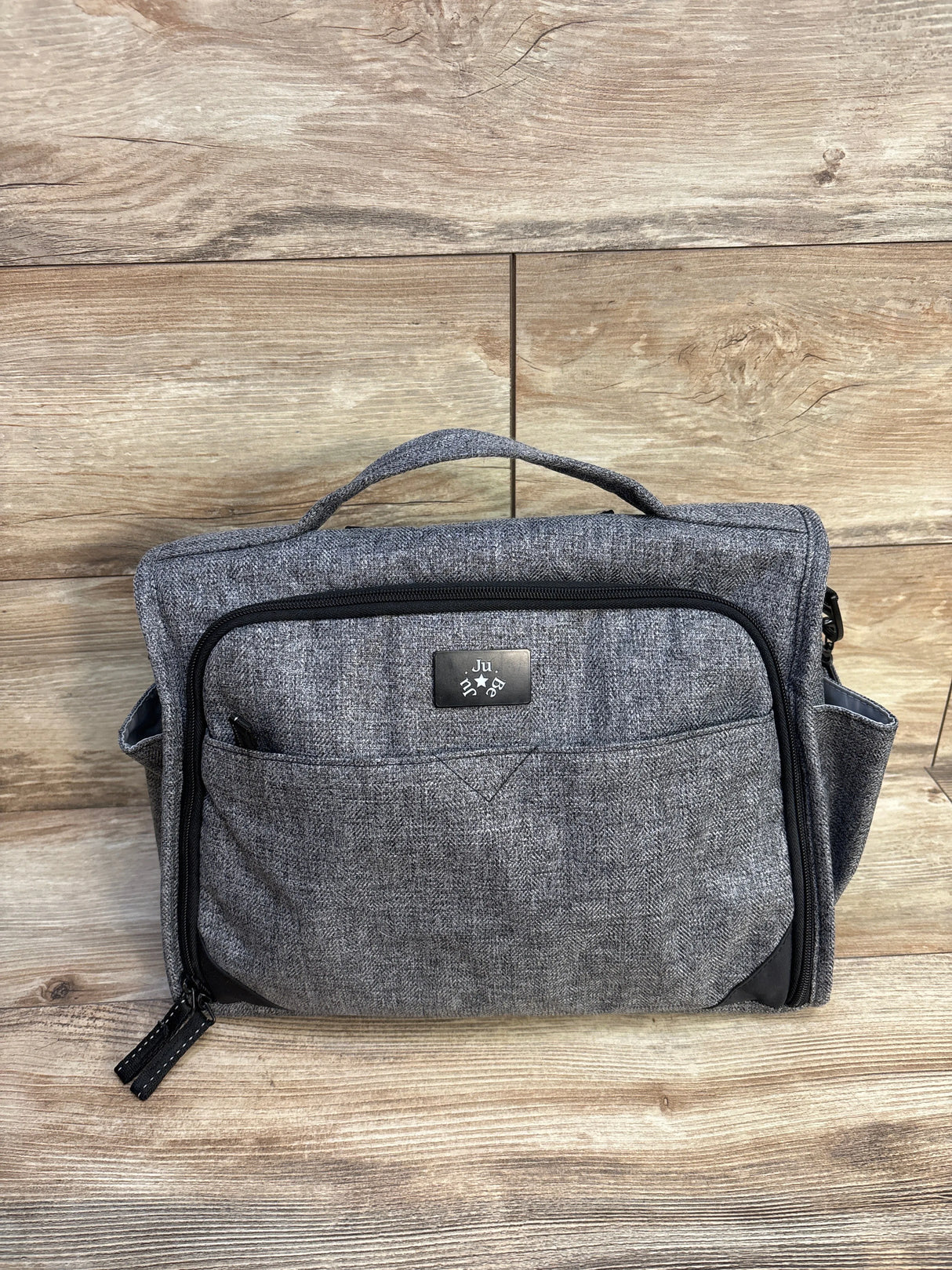 Gray fabric diaper bag with front zipper pocket on wood background