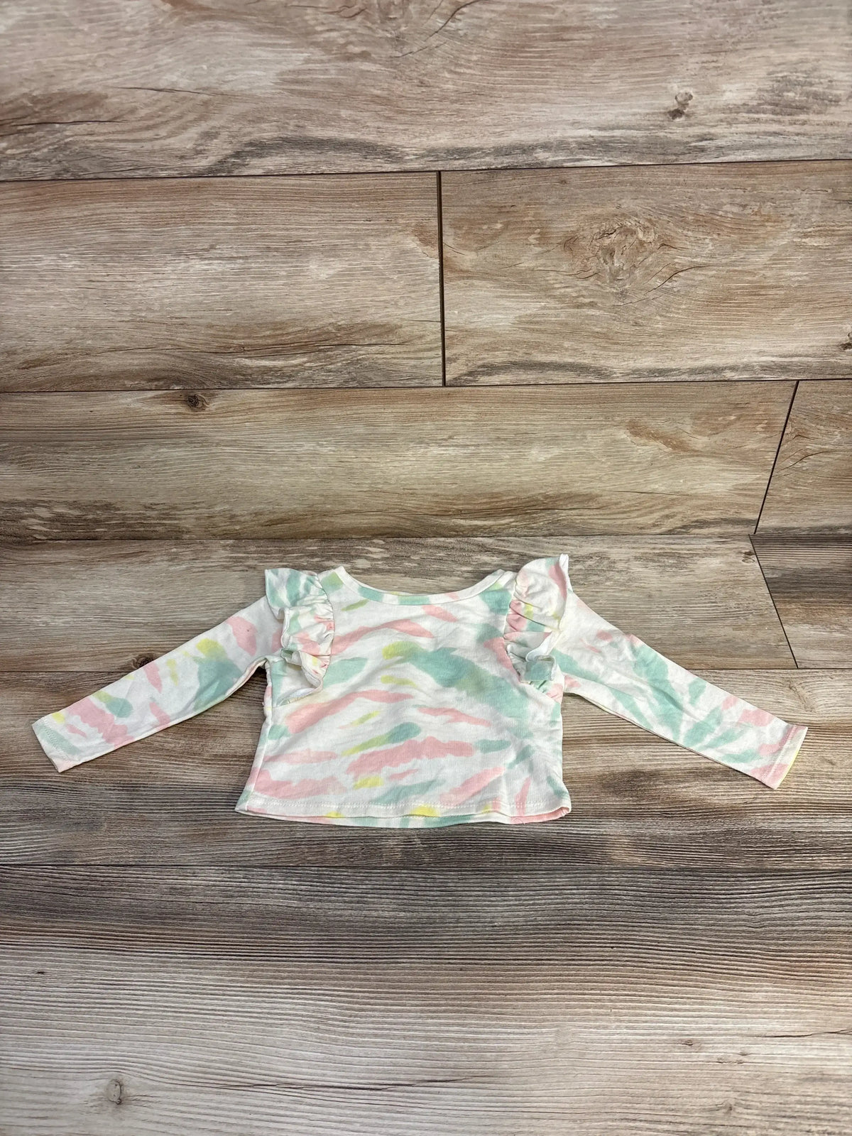 Flat lay of Grayson tie-dye flutter sleeve baby top, 12m, showing pastel pink, green, and yellow pattern with ruffle shoulders on wood floor