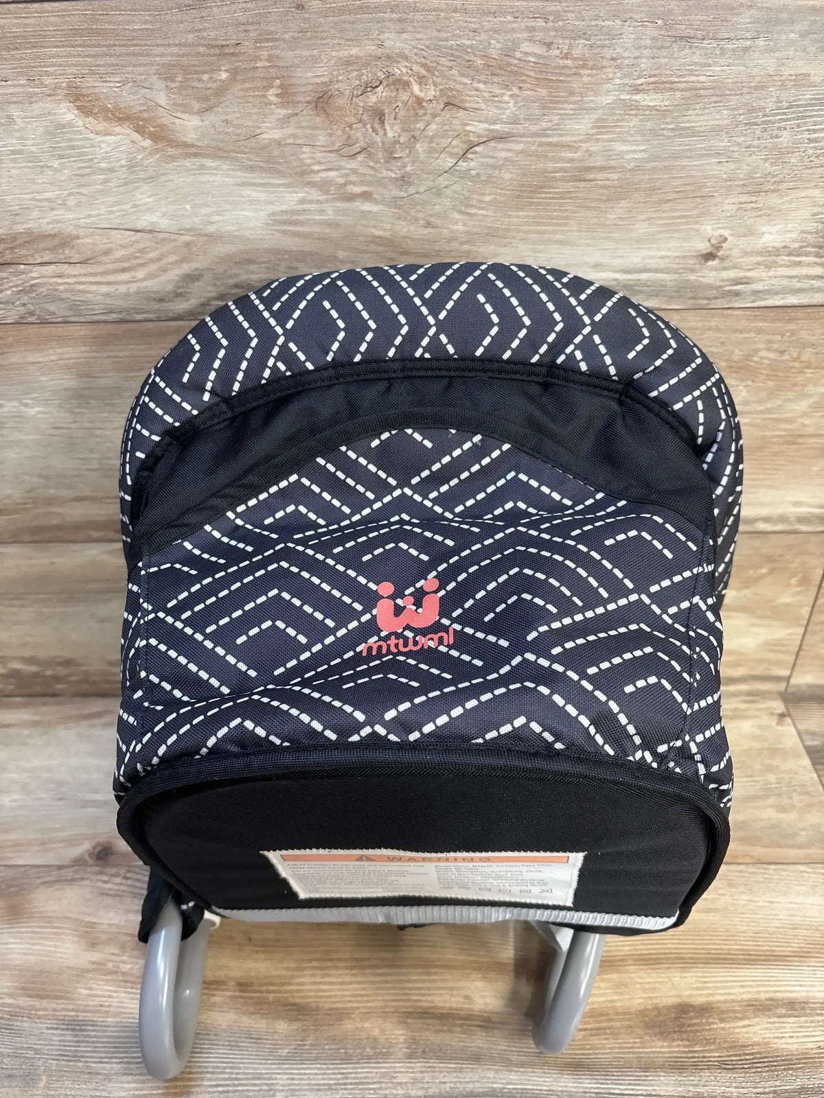 Front view of MTWML Hook On High Chair in black with white geometric stripe pattern and red logo on wood plank floor