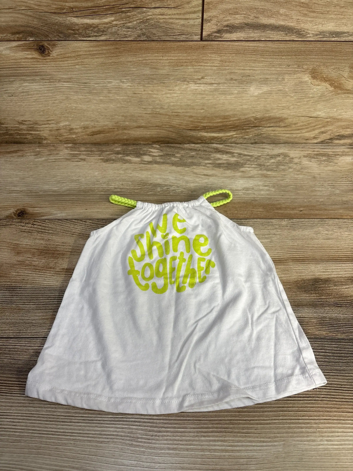 Flat lay of white toddler halter top with neon braided straps and we shine together print on wood background