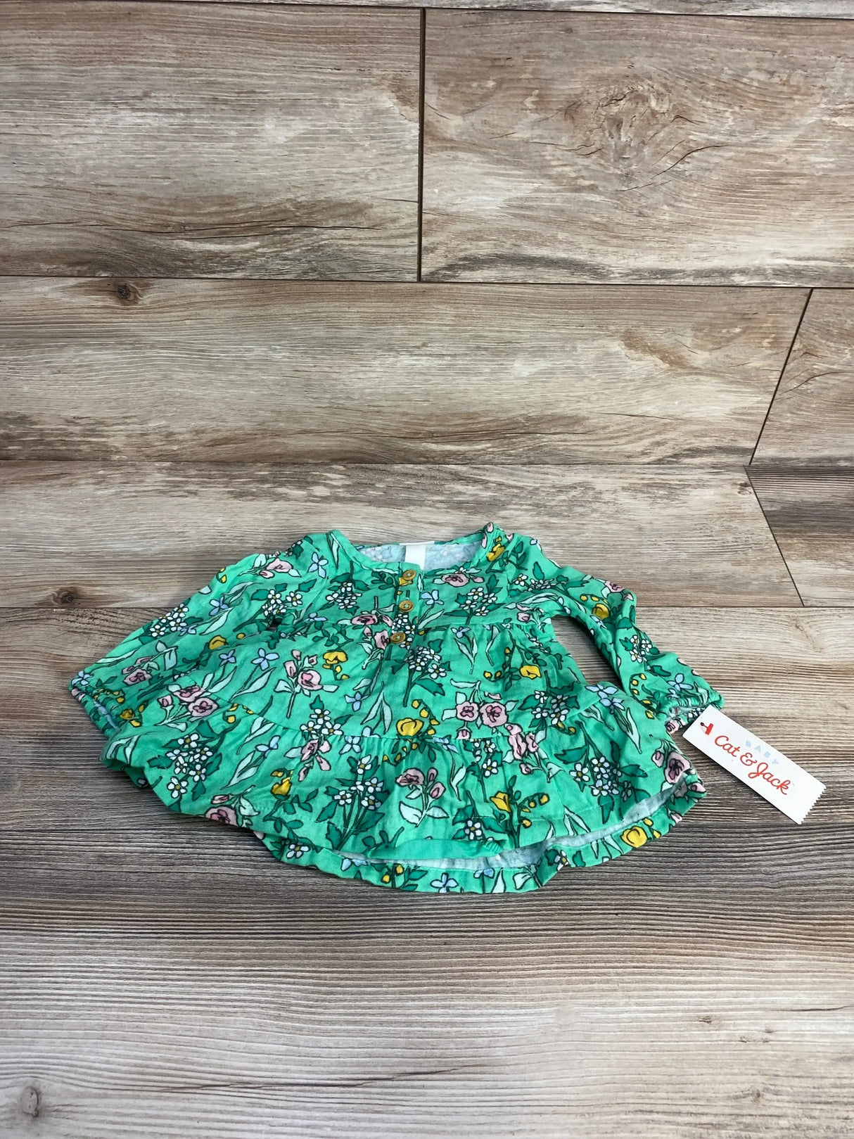 Top-down view of Cat & Jack green floral henley dress with bloomers, ruffled tiered skirt and front buttons on wood floor