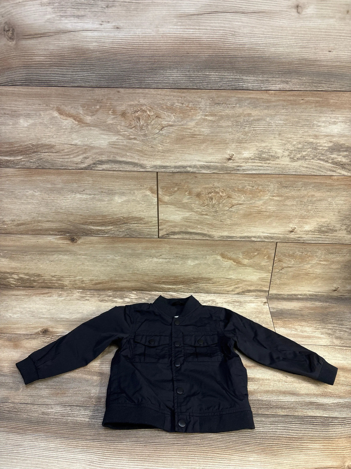 Flat lay front of Cat and Jack black toddler utility jacket with snap buttons and chest flap pockets on wood background