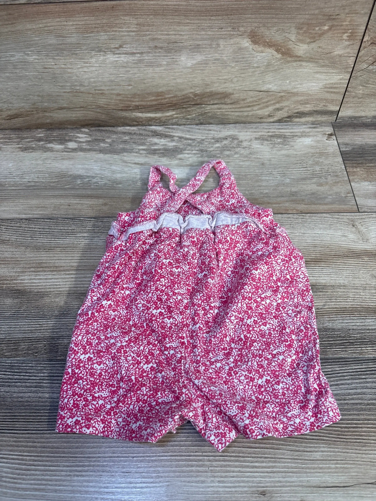 Flat lay of Carter’s pink floral tank romper size 6 months showing crisscross back straps and ruffled waist on wood floor