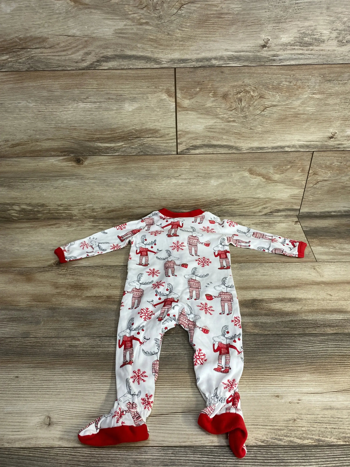 Baby Christmas pajamas with reindeer and snowflakes, red trim, footed design on wood floor