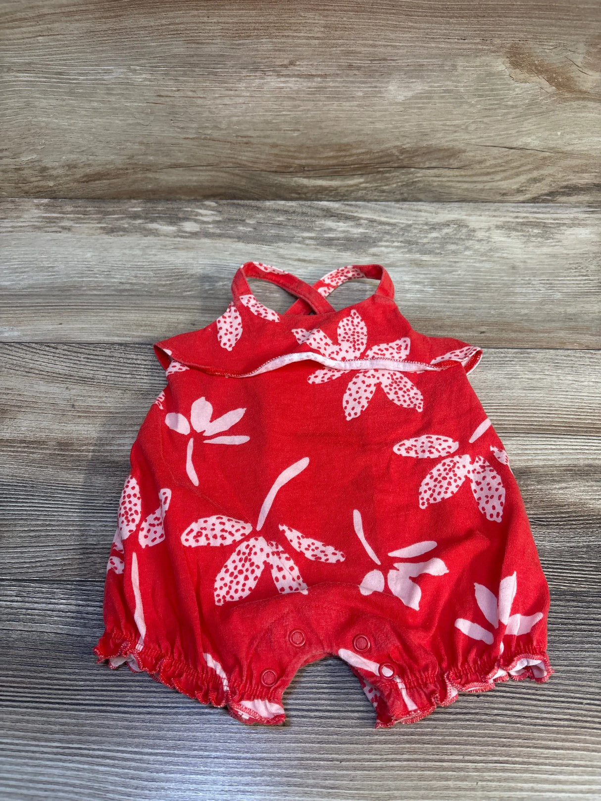 Flat lay of red floral shortie romper size 3M with crisscross straps ruffle trim and snap crotch on wood background