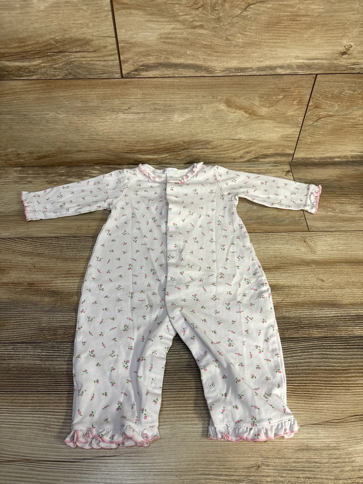 Front view of Kissy Kissy floral ruffle sleeper showcasing pink-trimmed ruffles and snap closures on a wood floor
