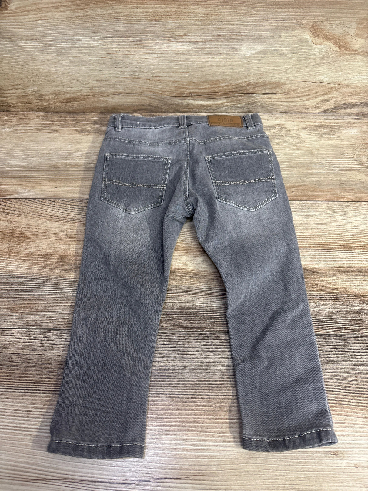 Gray kids jeans with back pockets laid flat on wood background