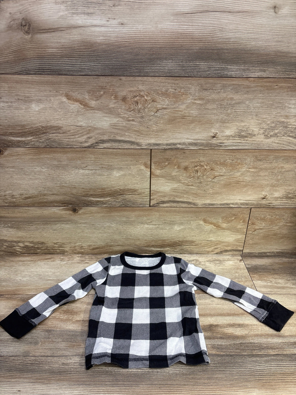 Front view of a black and white plaid thermal shirt showcasing long sleeves with a wood-patterned background
