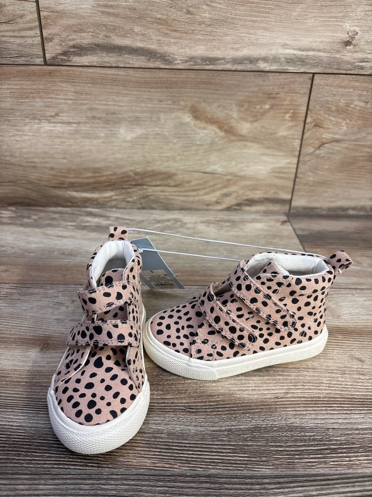 Pair of pink-beige leopard high-top baby sneakers with double velcro straps and white soles on wood background