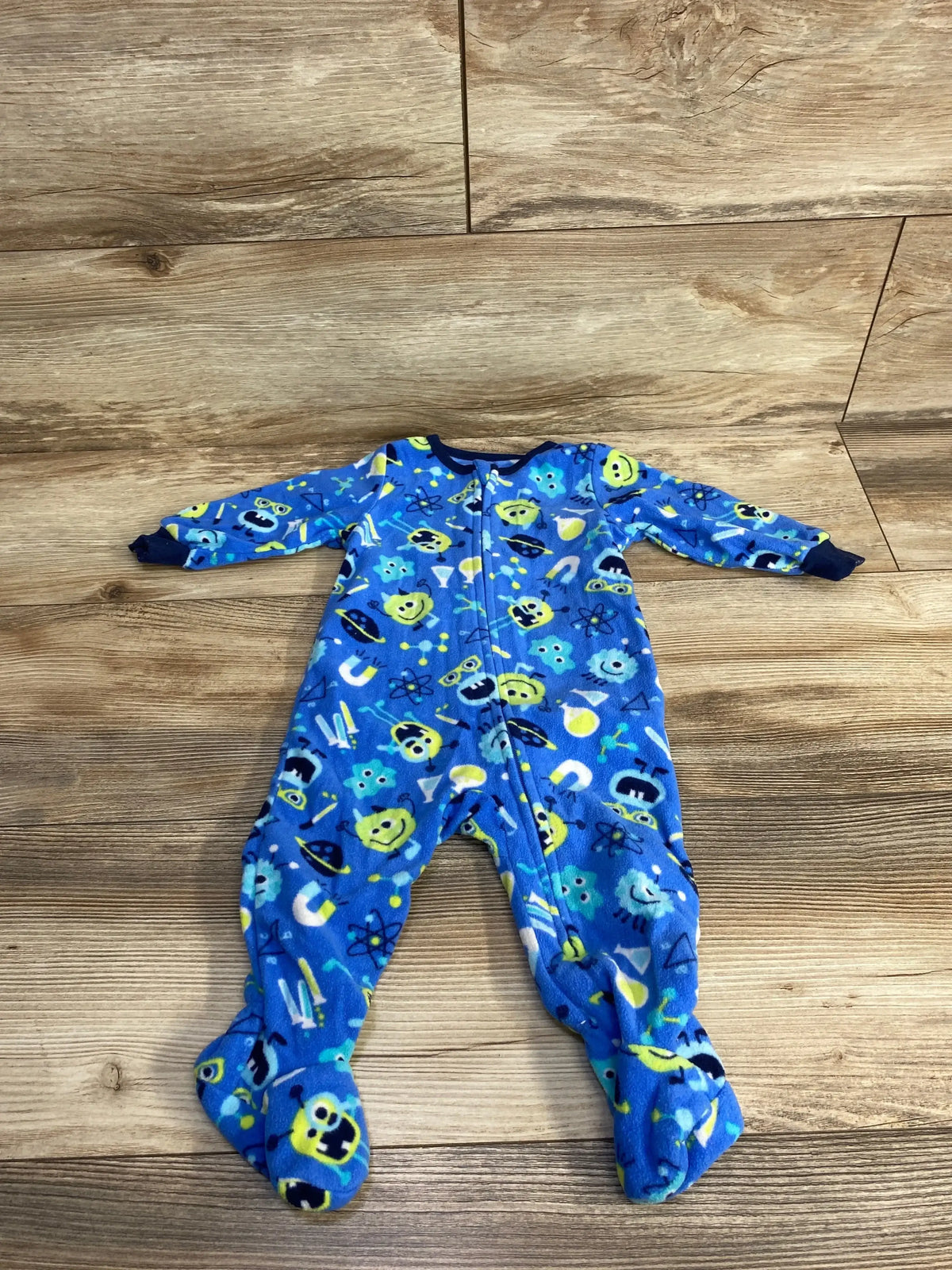 Blue fleece baby onesie with science-themed prints including atoms, magnets, and test tubes on wooden floor