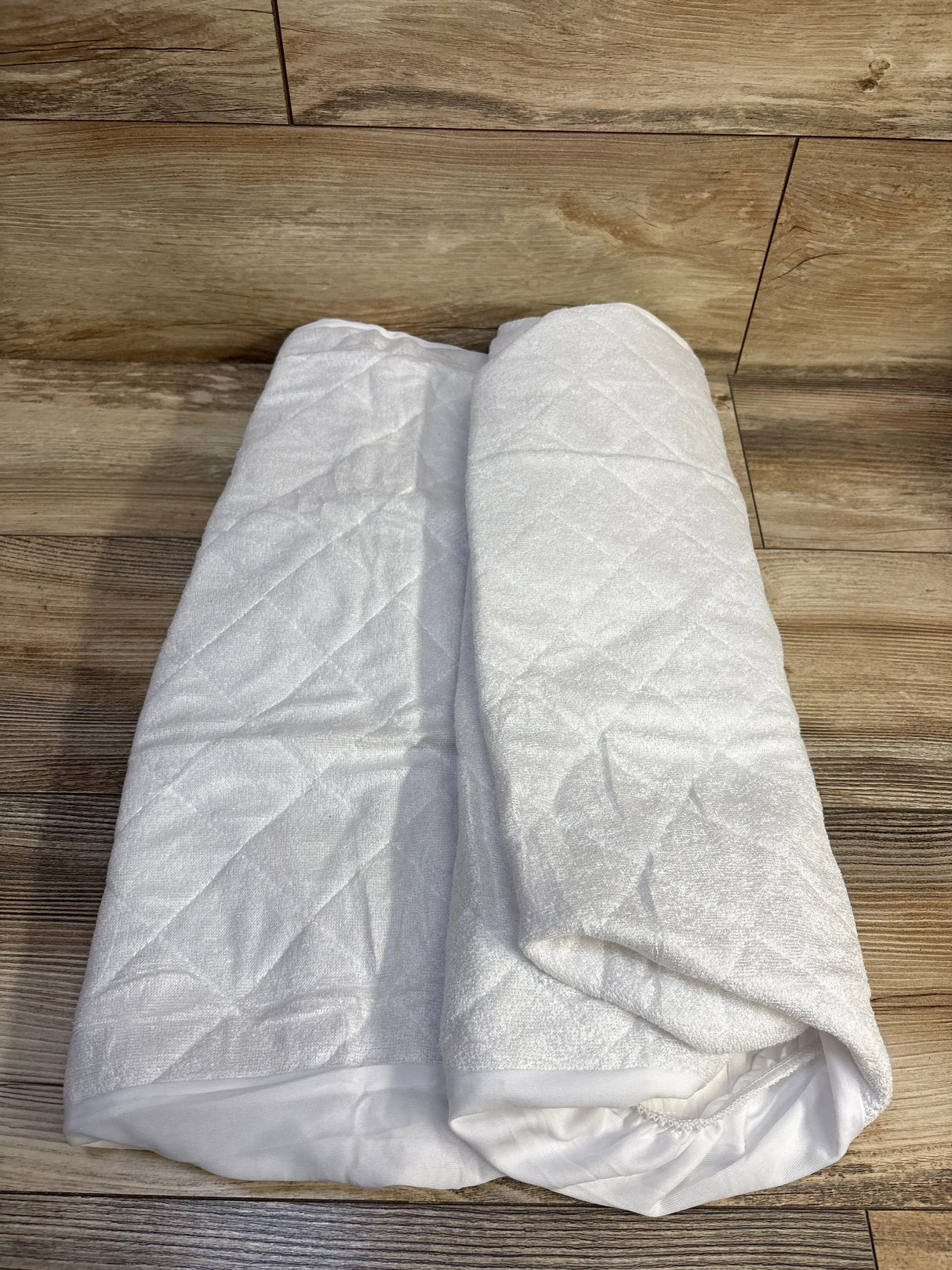 Folded view of two white quilted waterproof bassinet mattress covers (33x20 in) with diamond quilting on wood background