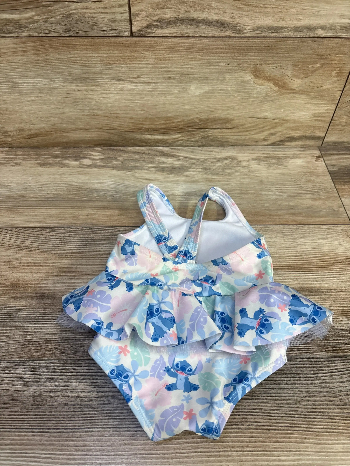 Back view of Disney Baby Stitch 1pc Tutu Swimsuit sz 9m showing crisscross straps and blue and pink Stitch print ruffle skirt on wood plank floor