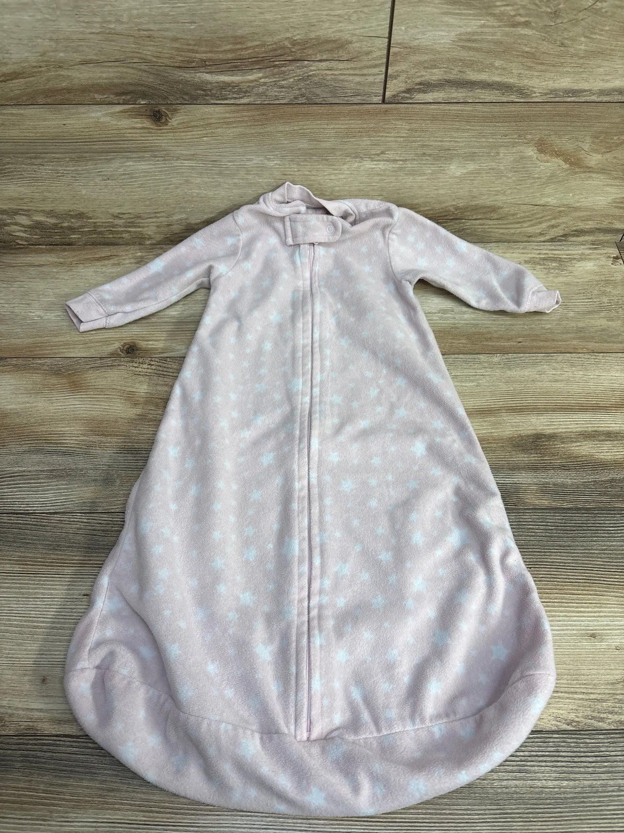 Light pink baby sleep sack with white star pattern and zipper on wooden surface