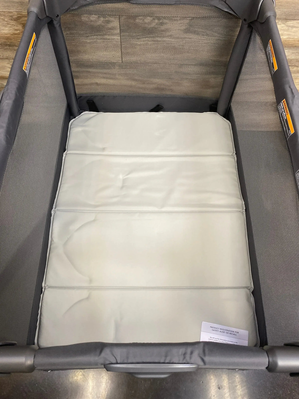 Top-down view of 4moms Breeze Go Playard in grey showing padded mattress insert and mesh side panels on wood floor