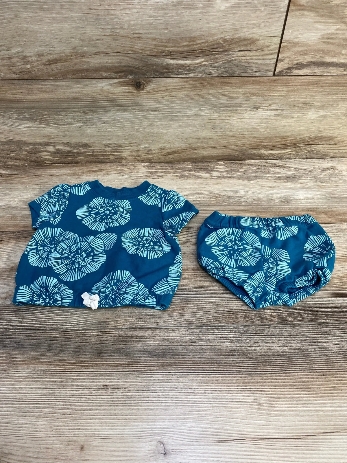 Flat lay of blue 2-piece baby set 6m showing short-sleeve floral top with white bow and matching elastic bloomers on wood