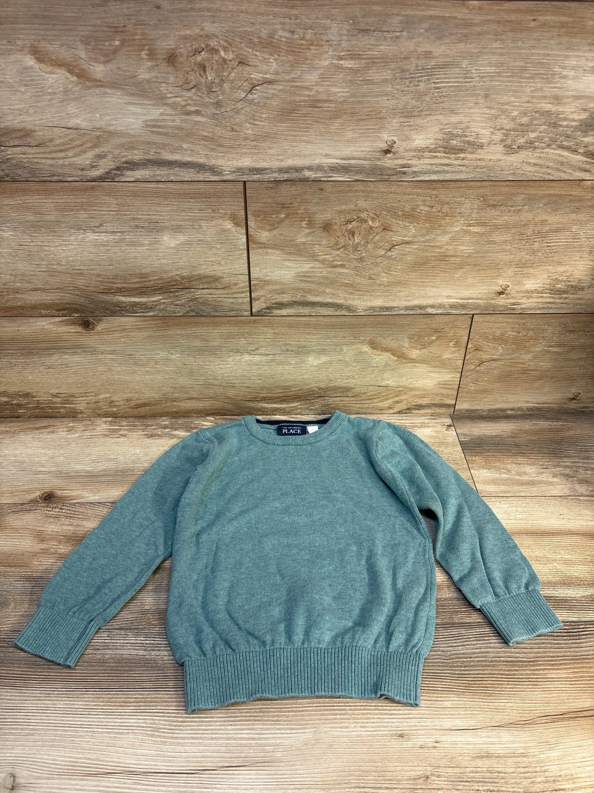 Front flat lay of teal Children's Place crew neck sweater size 5T showing ribbed cuffs and hem on wood background