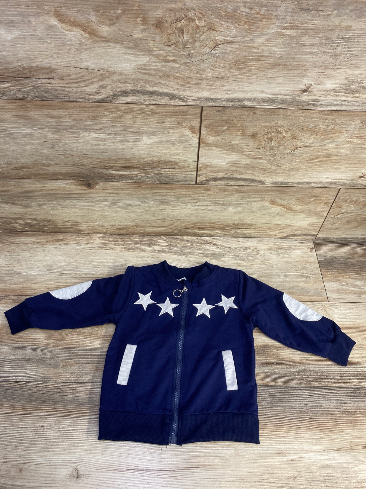Navy blue children's jacket with white star patches and elbow patches on wooden floor
