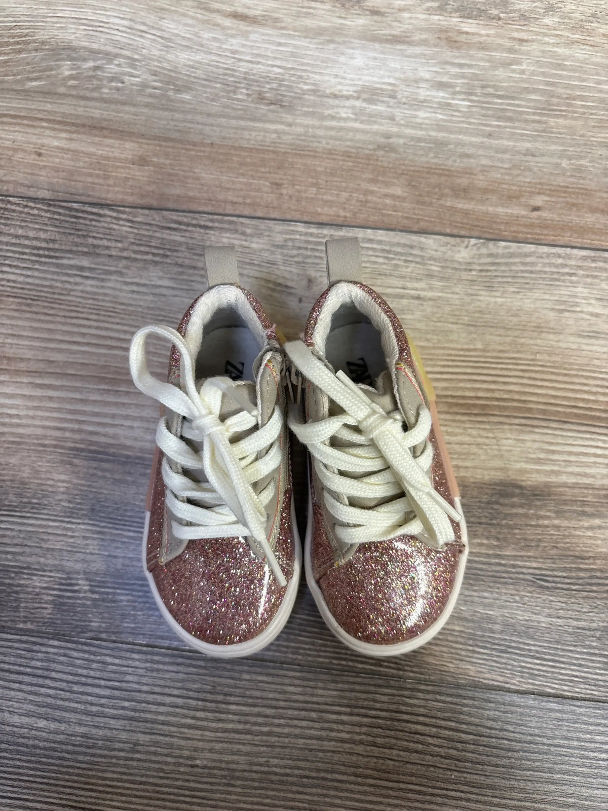 Top view of Zara pink glittery high top sneakers showcasing white laces and pull tabs on a wood floor