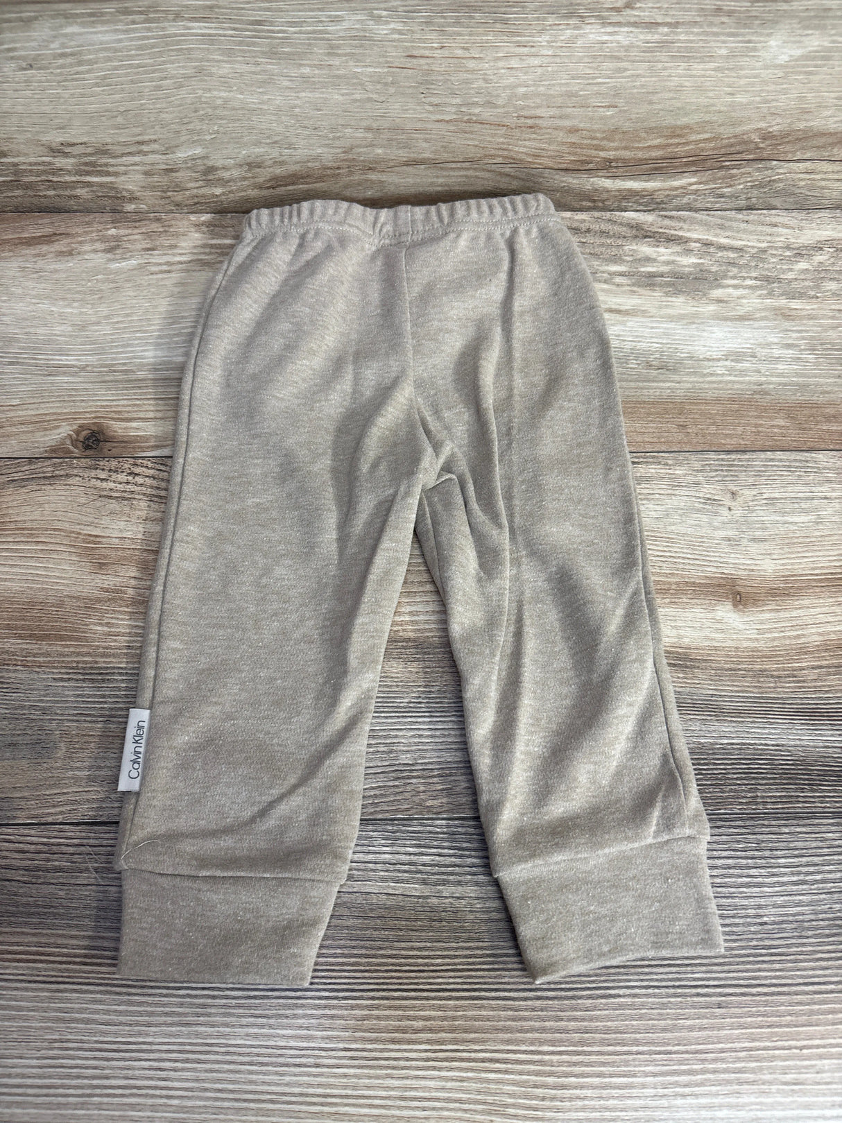 Light beige Calvin Klein baby pants with elastic waist on wooden background