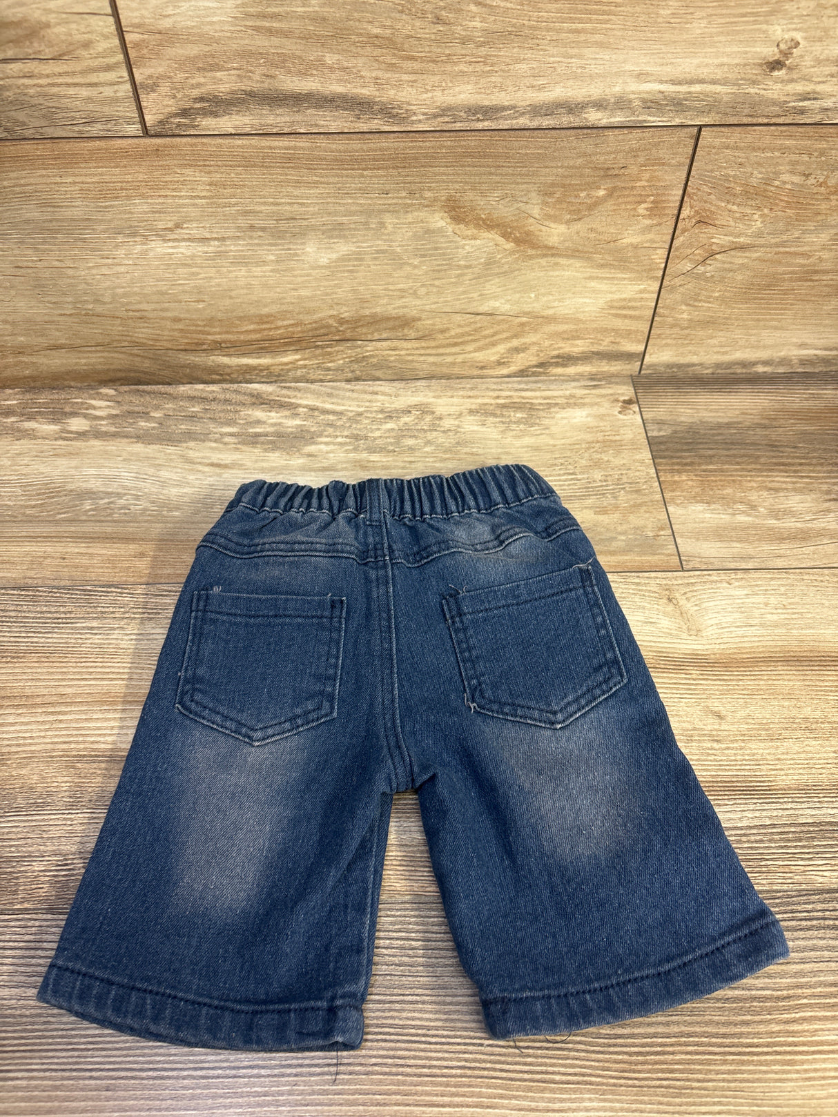 Back view of toddler blue distressed denim shorts size 2T showcasing elastic waistband and two back patch pockets on a wood floor