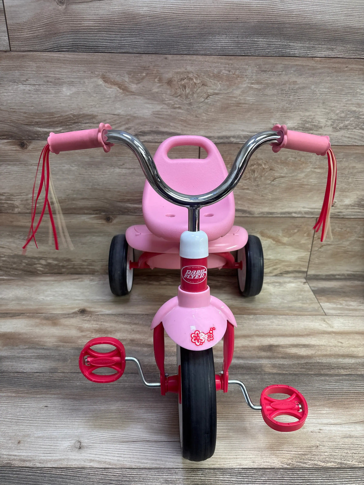 Front view of pink Radio Flyer Ready to Ride Folding Trike with chrome handlebars, red pedals, and tassels