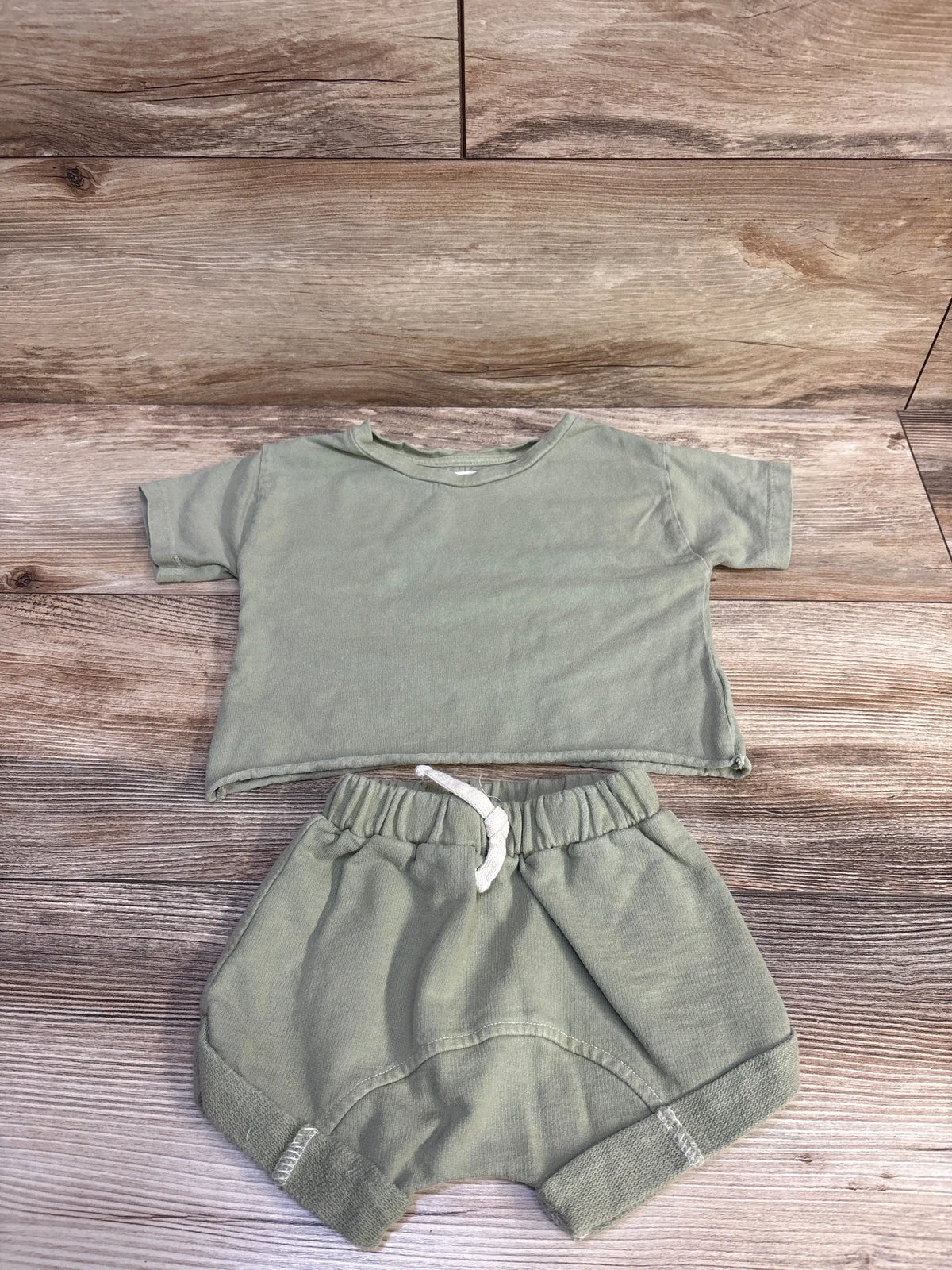 Top-down view of green Little Wild 2pc shirt and shorts set with short sleeves and drawstring waist on wood-look floor