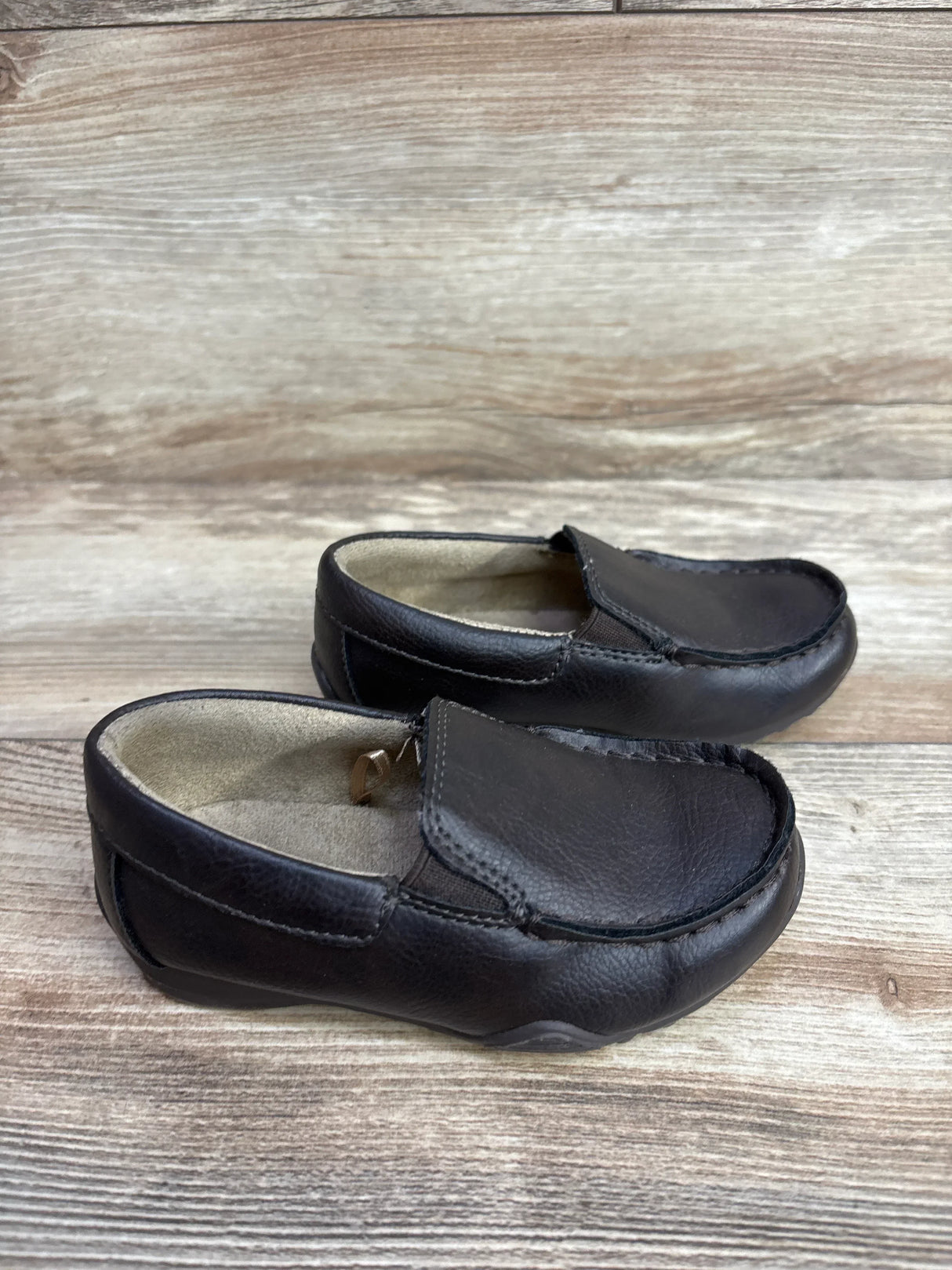 Three-quarter view of Children's Place brown slip-on dress shoes size 8C showing leather upper and soft lining on wood background