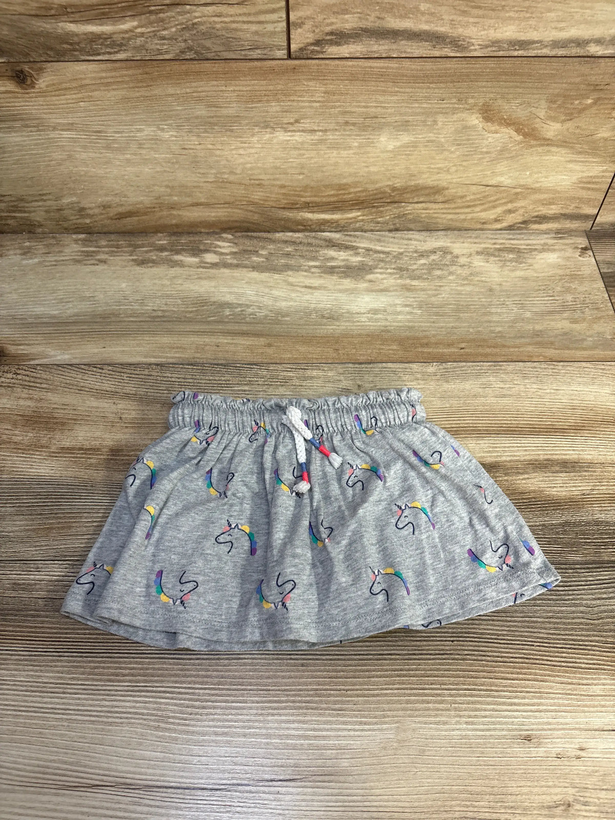 Front view of a grey Cat & Jack drawstring skort showcasing unicorn print and elastic waist on a wood-grain surface