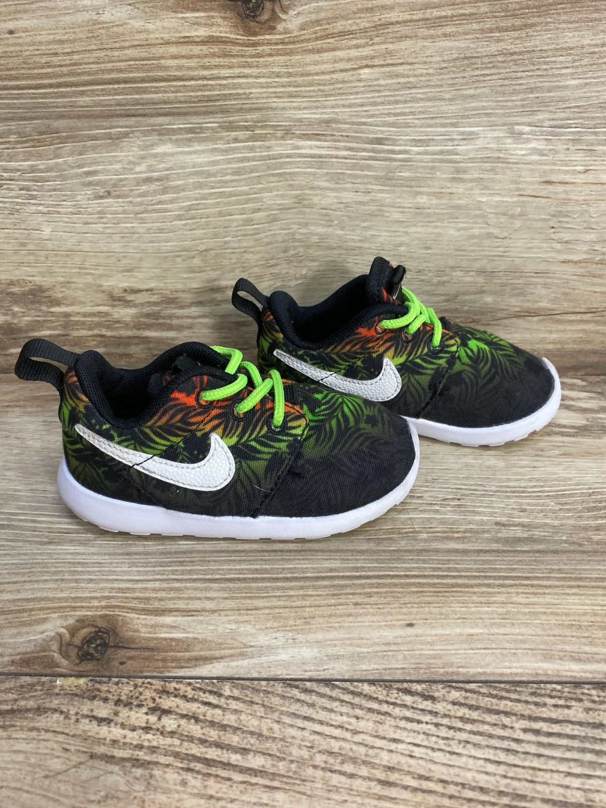 Side view of Nike Roshe Run sneaker size 5C with green orange print, neon laces, white swoosh on wood background