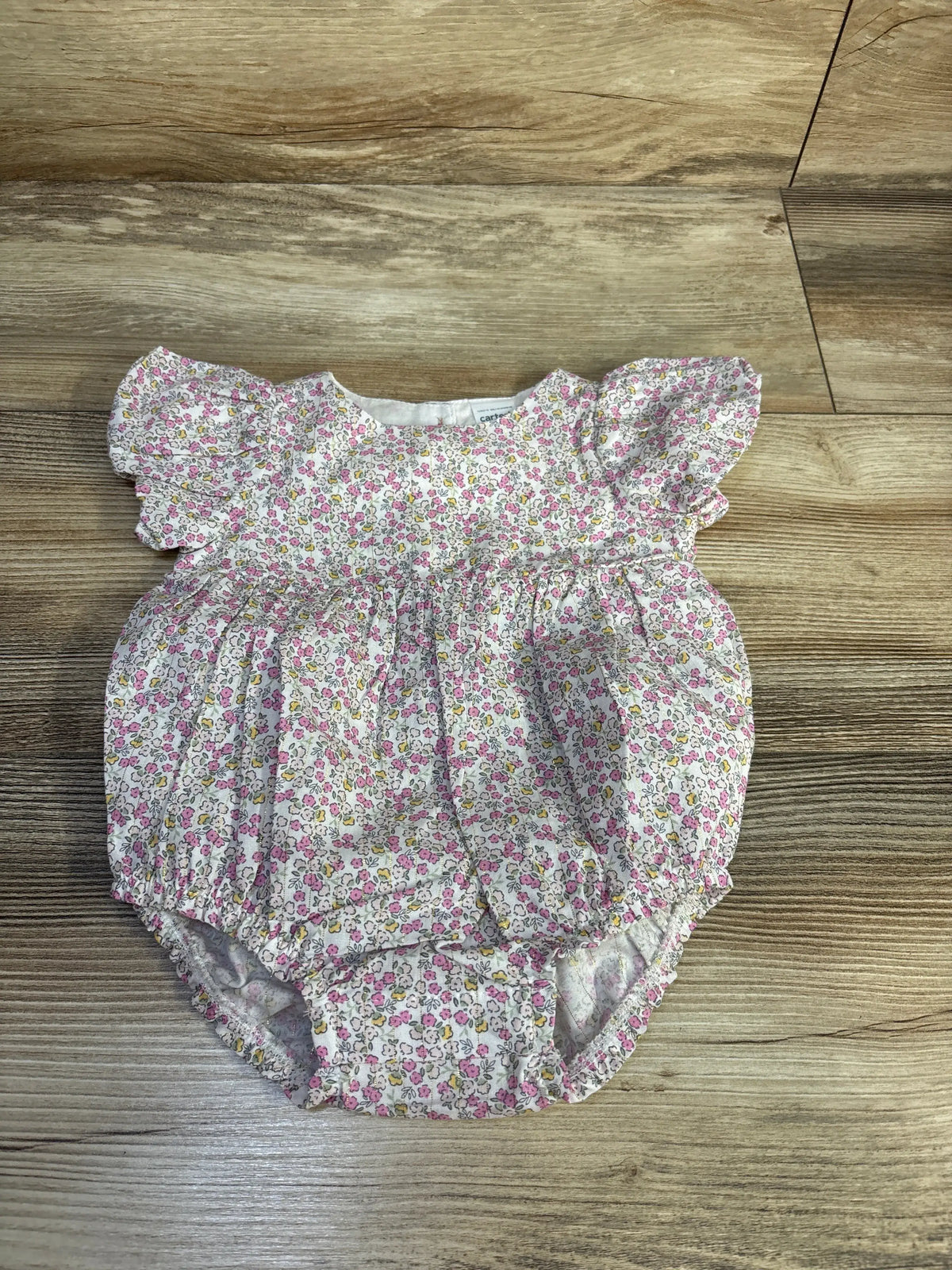 Top view of Child Of Mine white floral bubble romper in size 0-3 months showcasing gathered legs on a wood floor