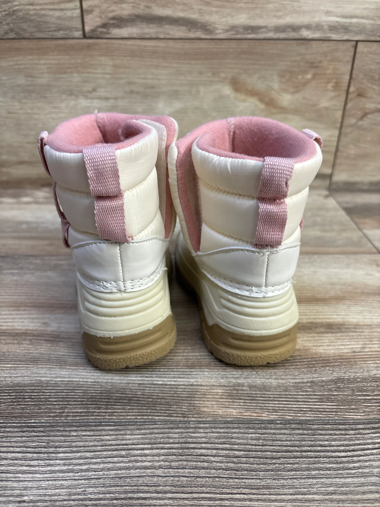 Rear view of Oshkosh toddler winter boots in ivory with pink lining and pull tabs, tan rubber soles on wood floor
