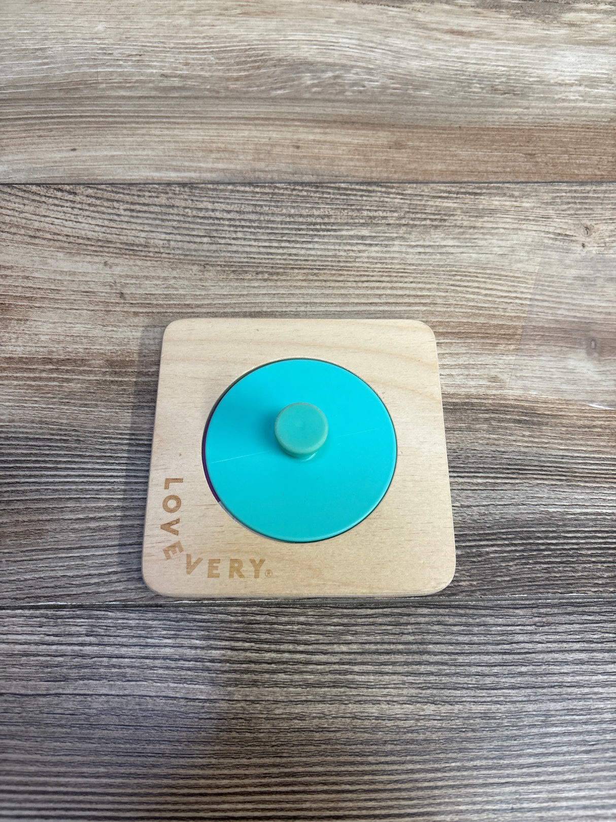 Lovevery wooden puzzle with teal circle knob on wood grain surface