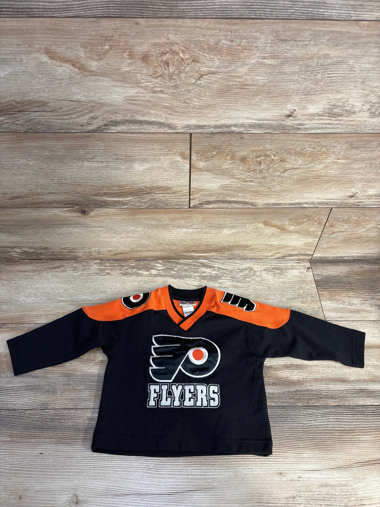 Black and orange Philadelphia Flyers hockey jersey with logo and text on front, flat on wooden floor