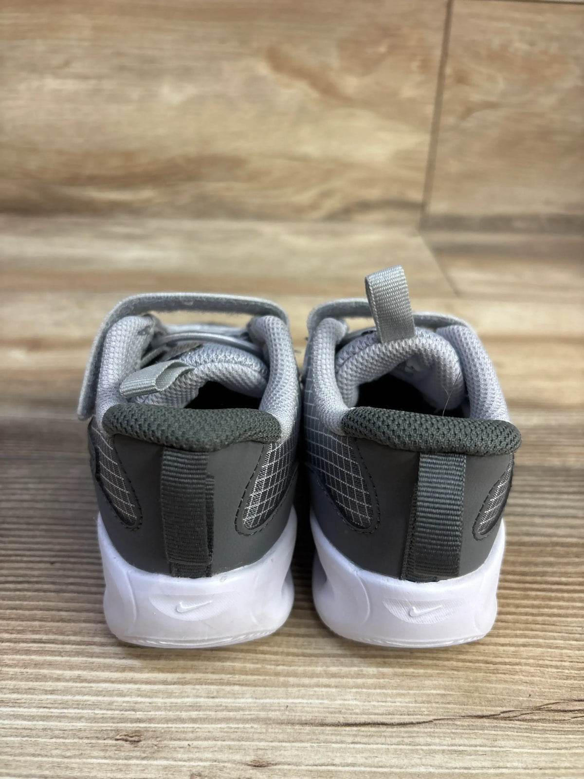 Rear view of Nike Air Max Nova TD toddler sneakers showcasing Wolf Grey uppers and white cushioned soles on a wood surface