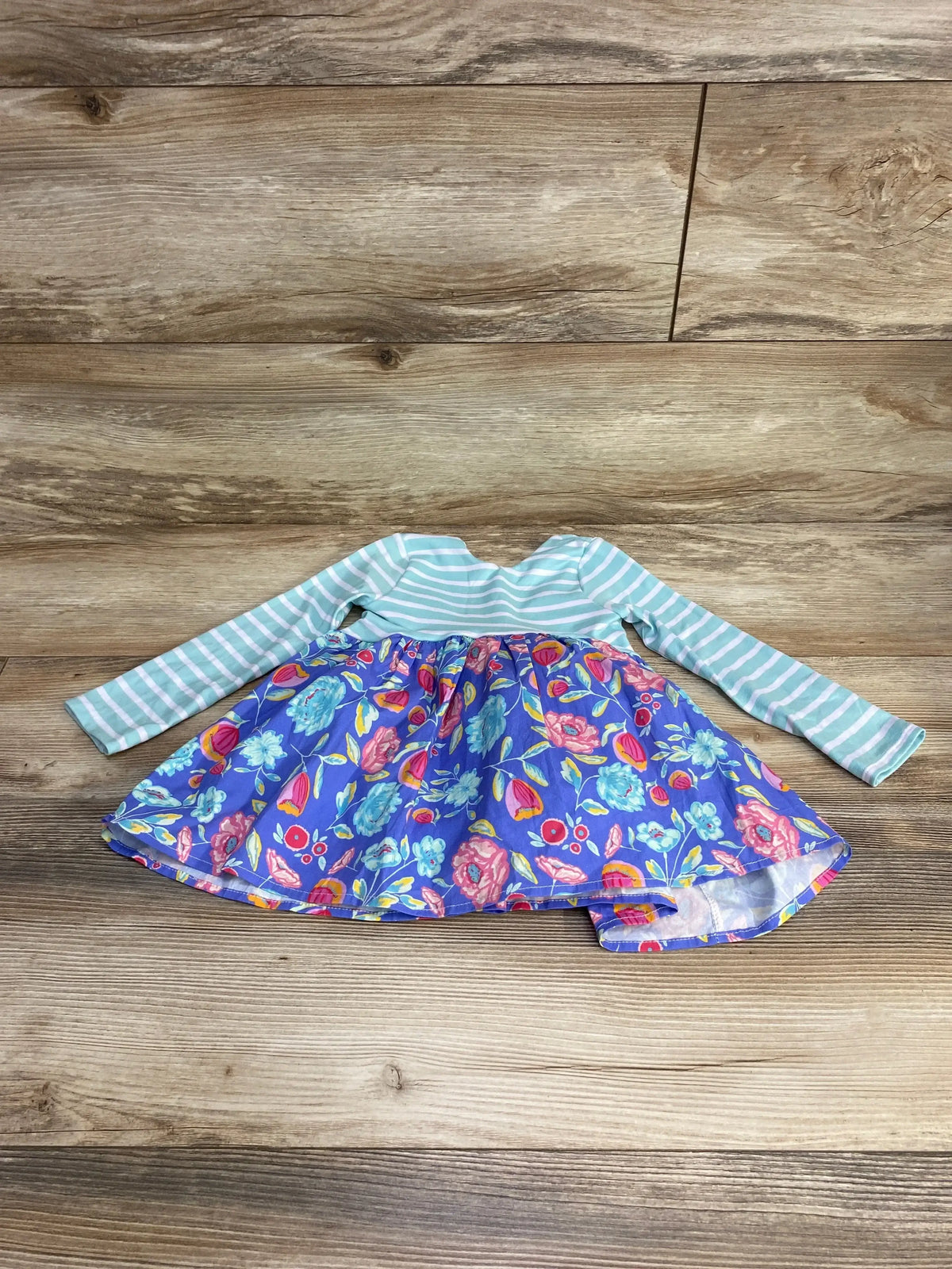 Flat lay of handmade baby dress with mint striped sleeves and blue floral skirt, gathered waist on wood background