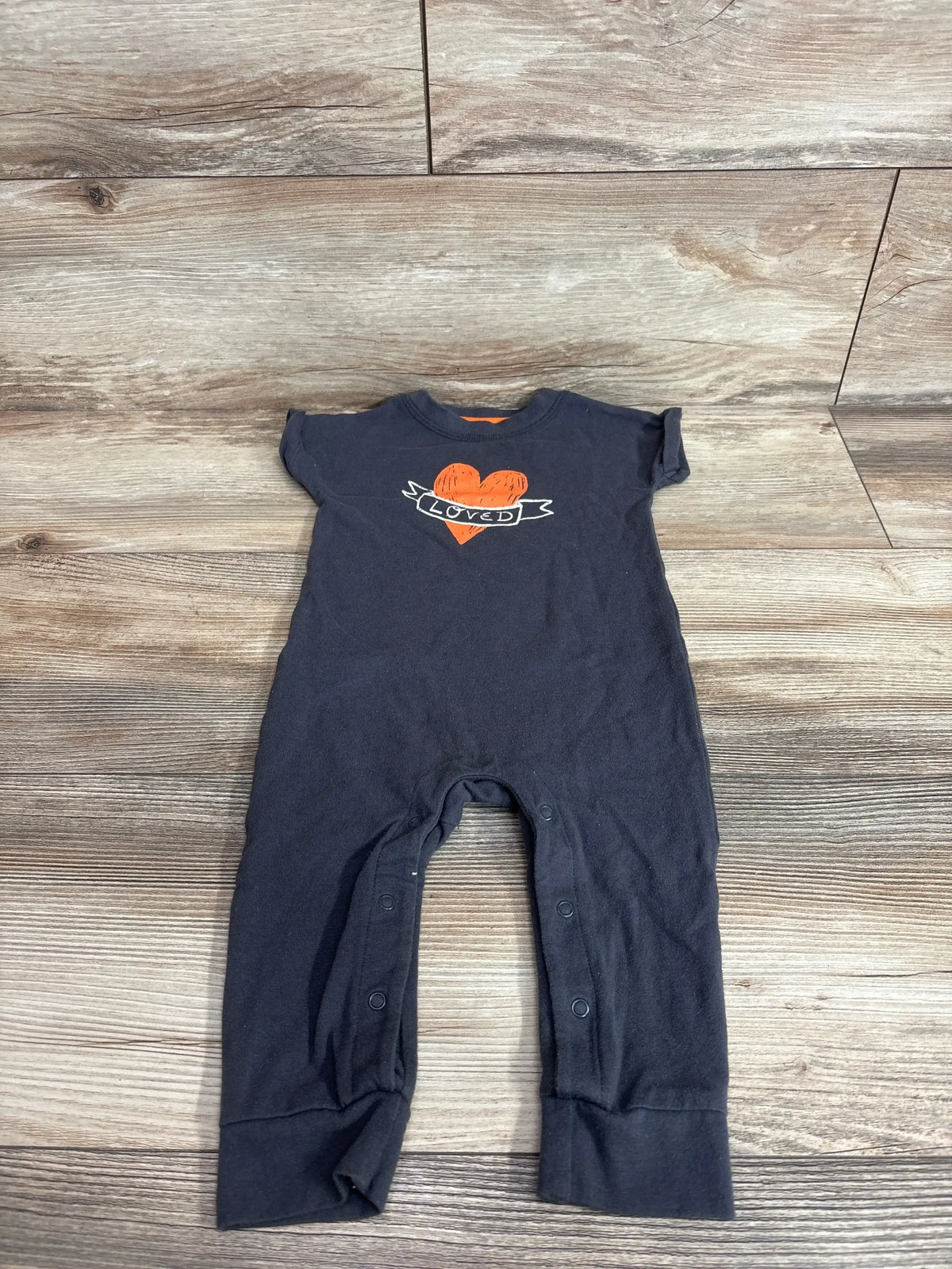Front view of Cat and Jack gray baby jumpsuit with orange heart Loved graphic and snap leg openings on wood background