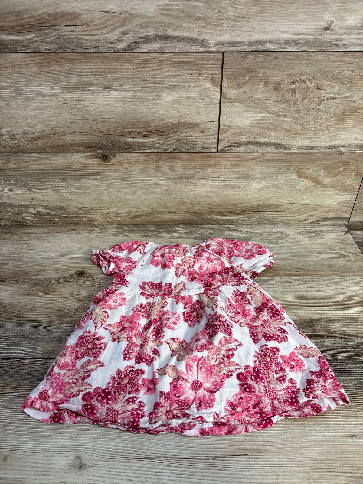 Flat lay of Old Navy pink floral layered baby dress size 18-24 months showing short puff sleeves and gathered tiered skirt on wood background