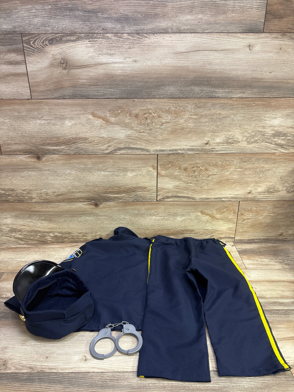 Top view of navy police officer costume with cap, shirt, striped pants, and toy handcuffs on a wood floor