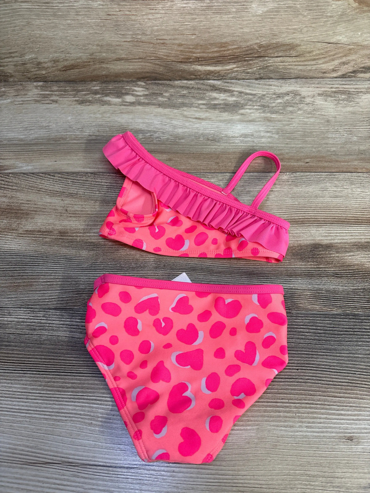 Top view of Cat & Jack pink two-piece swimsuit, size 18 months, with ruffled trim and heart pattern on wood grain
