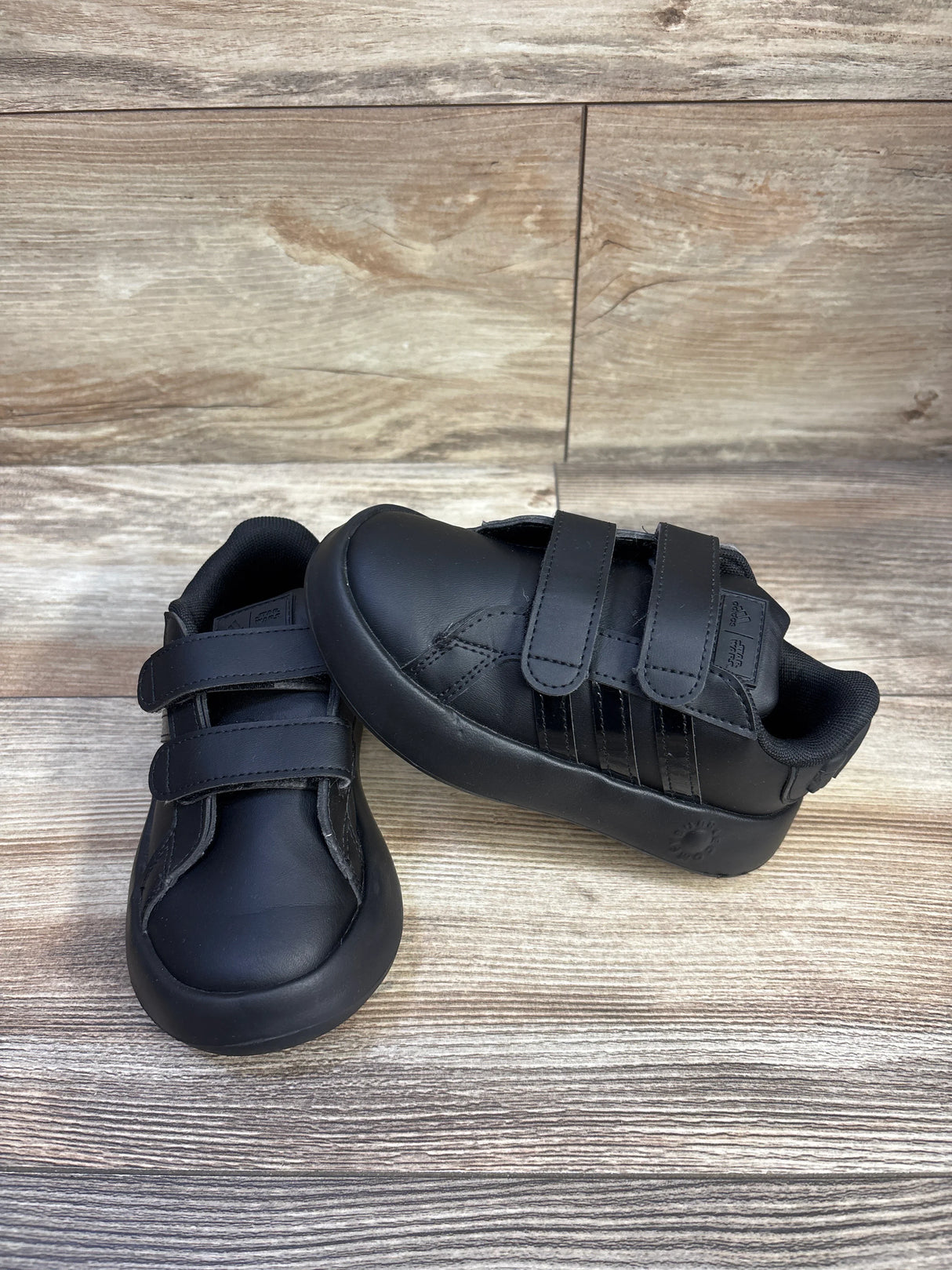 Angled view of Adidas x Star Wars black toddler Bubblecomfy sneaker showing double hook-and-loop straps and three side stripes on wood background