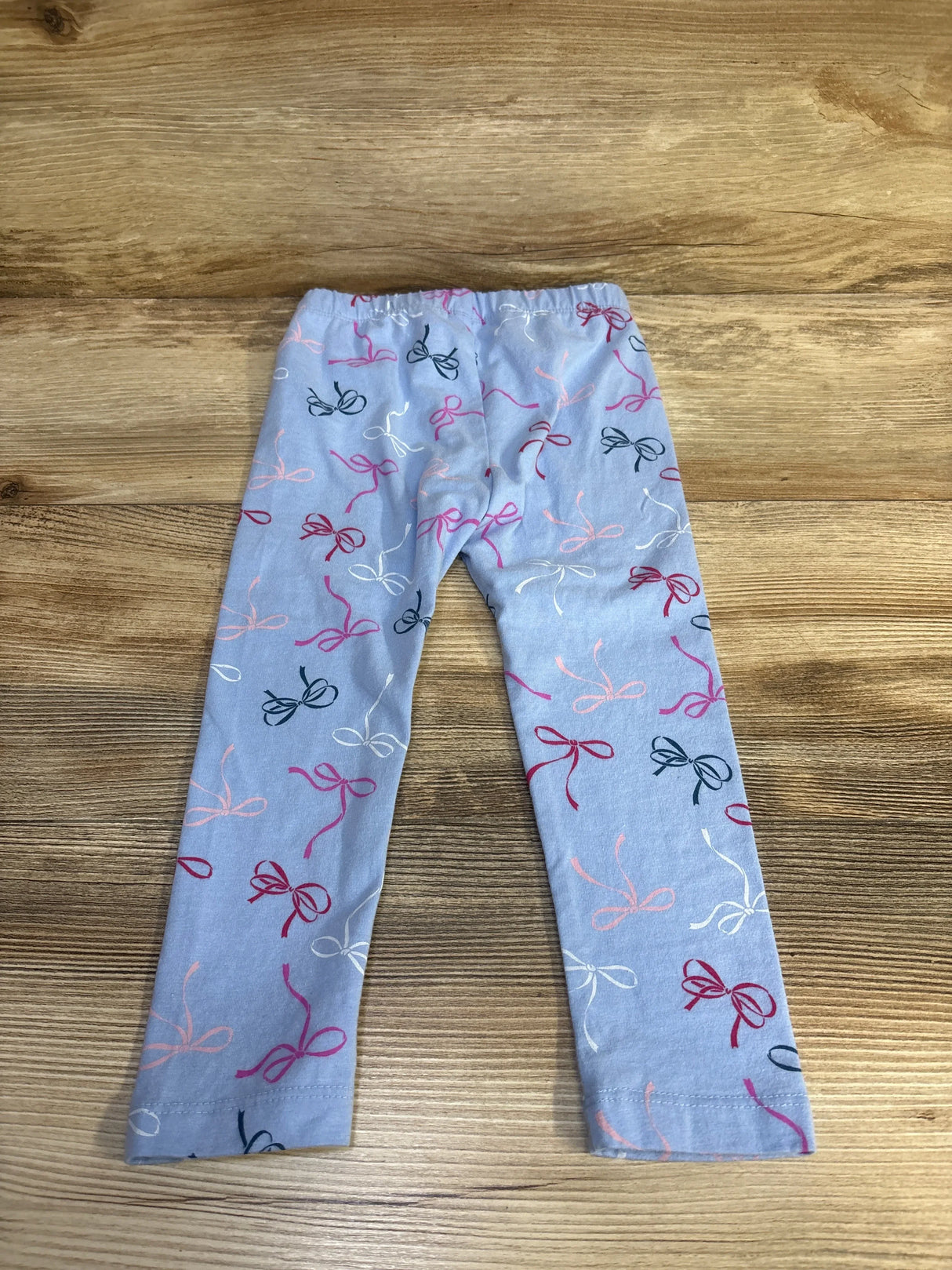 Flat lay of blue Baby Gap 2T toddler leggings showcasing all-over pink and navy bow print on wood background