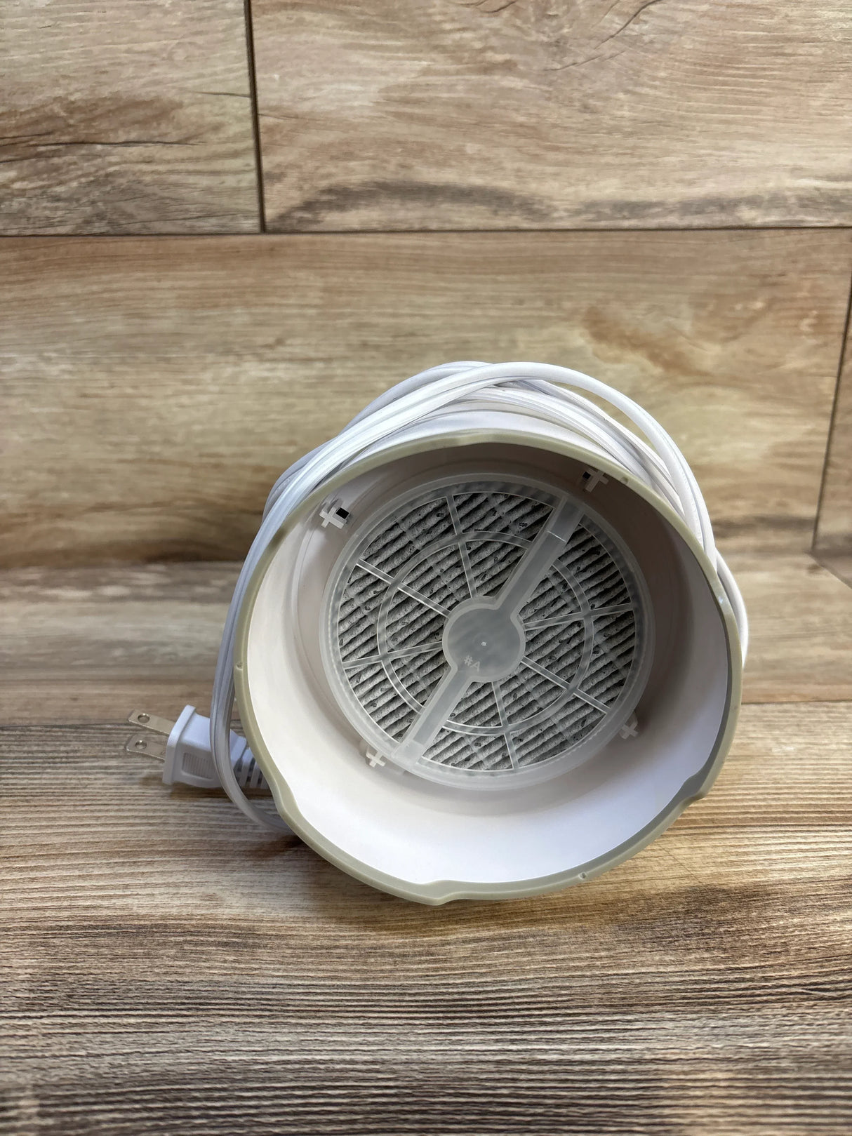 Front view of Frida Baby 3-in-1 air purifier showing round interior filter and wrapped power cord on wood background