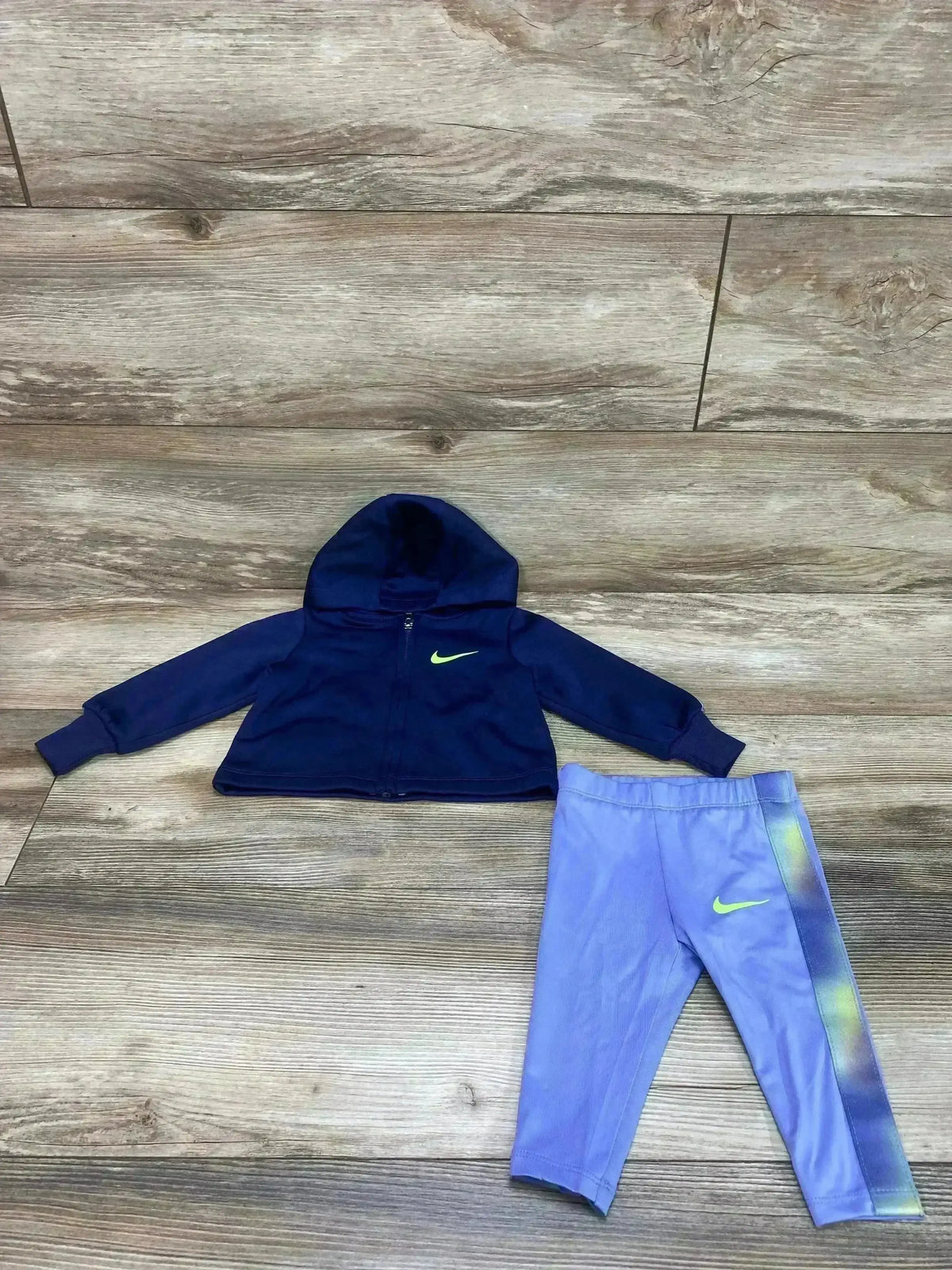 Flat lay of Nike navy zip hoodie and light purple leggings with neon green Swoosh, size 6 months on wood floor