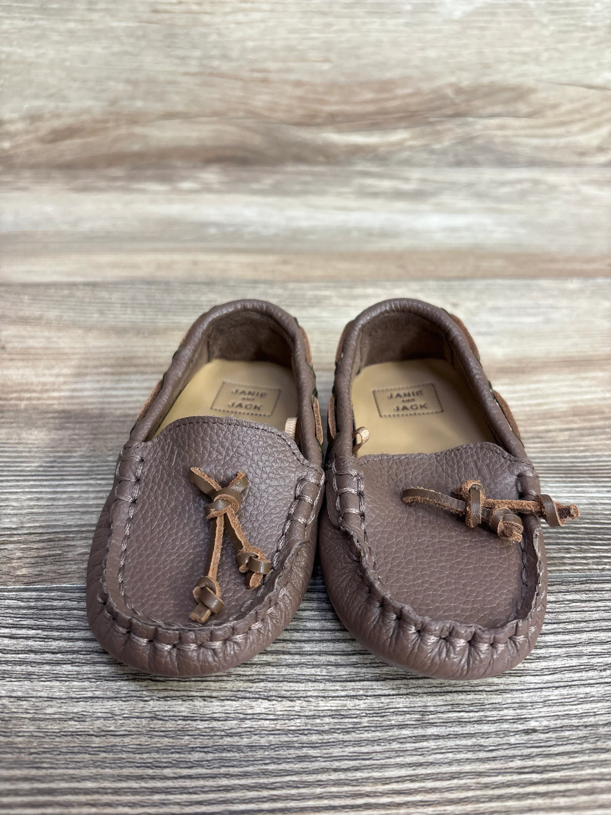 Front view of Janie and Jack brown leather driving shoes size 5C showcasing stitched moccasin toe and tied leather laces on light wood background