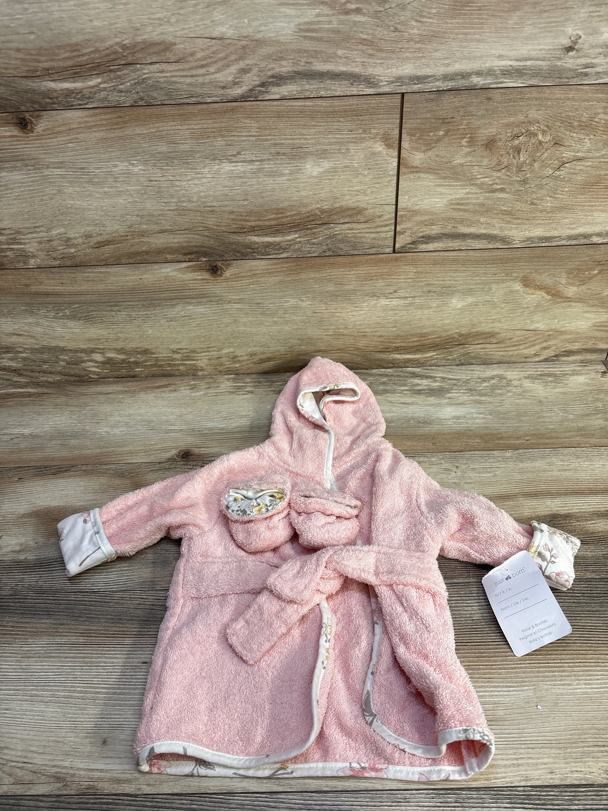 Flat lay of newborn pink hooded terry bath robe with matching booties, floral trim and tie belt on wood background