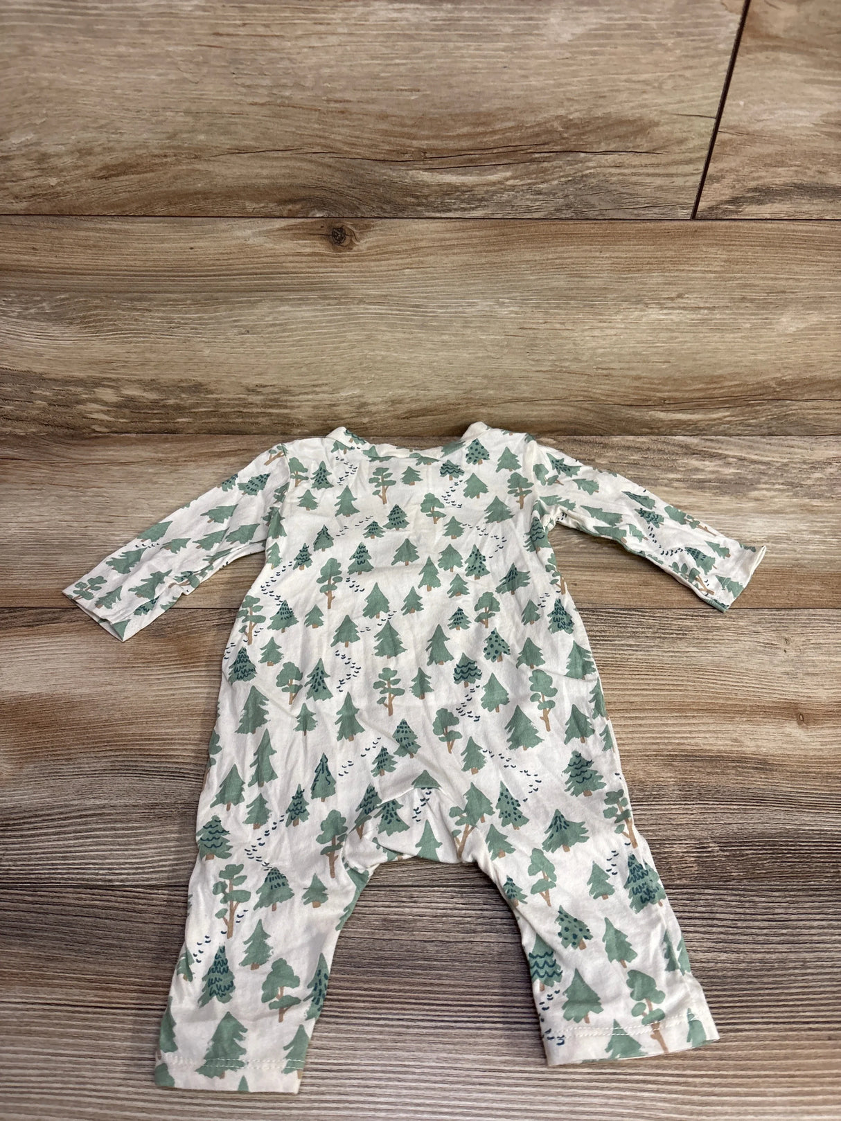 Baby romper with green tree pattern on white fabric laid on wooden floor